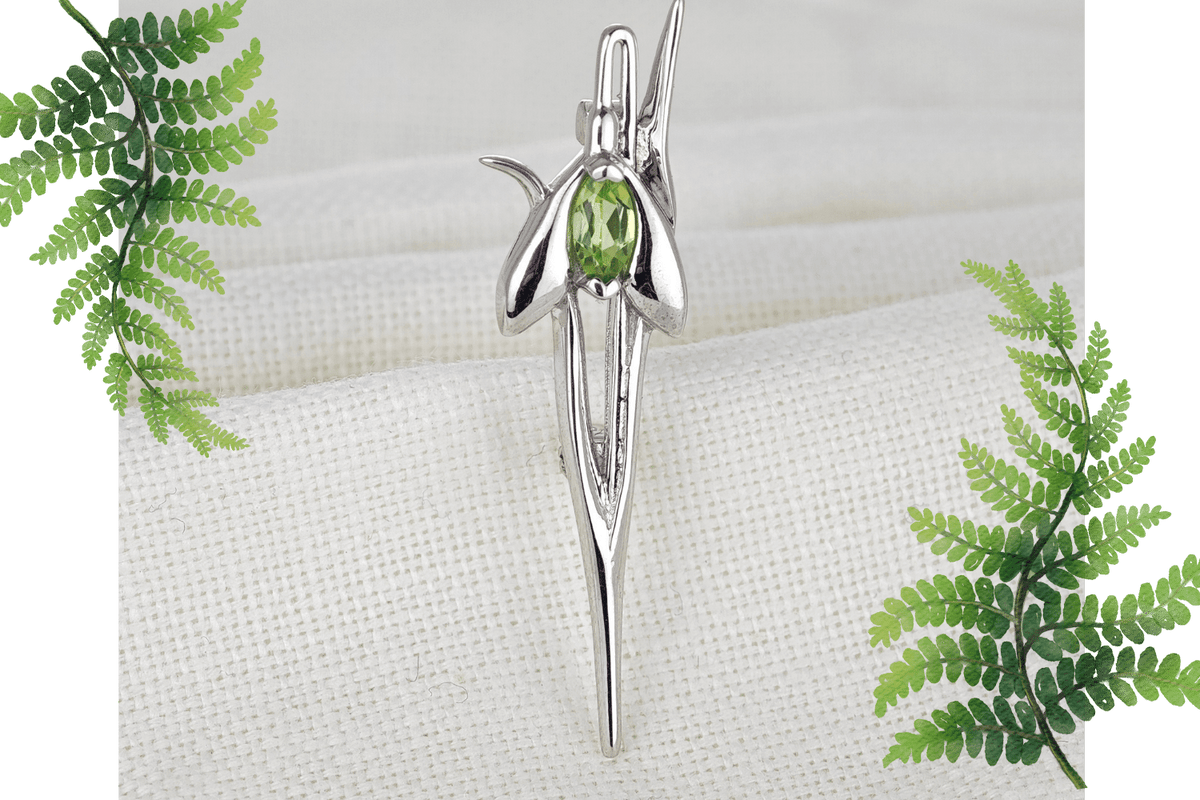 Peridot snowdrop silver brooch on natural fabric flagged by fern