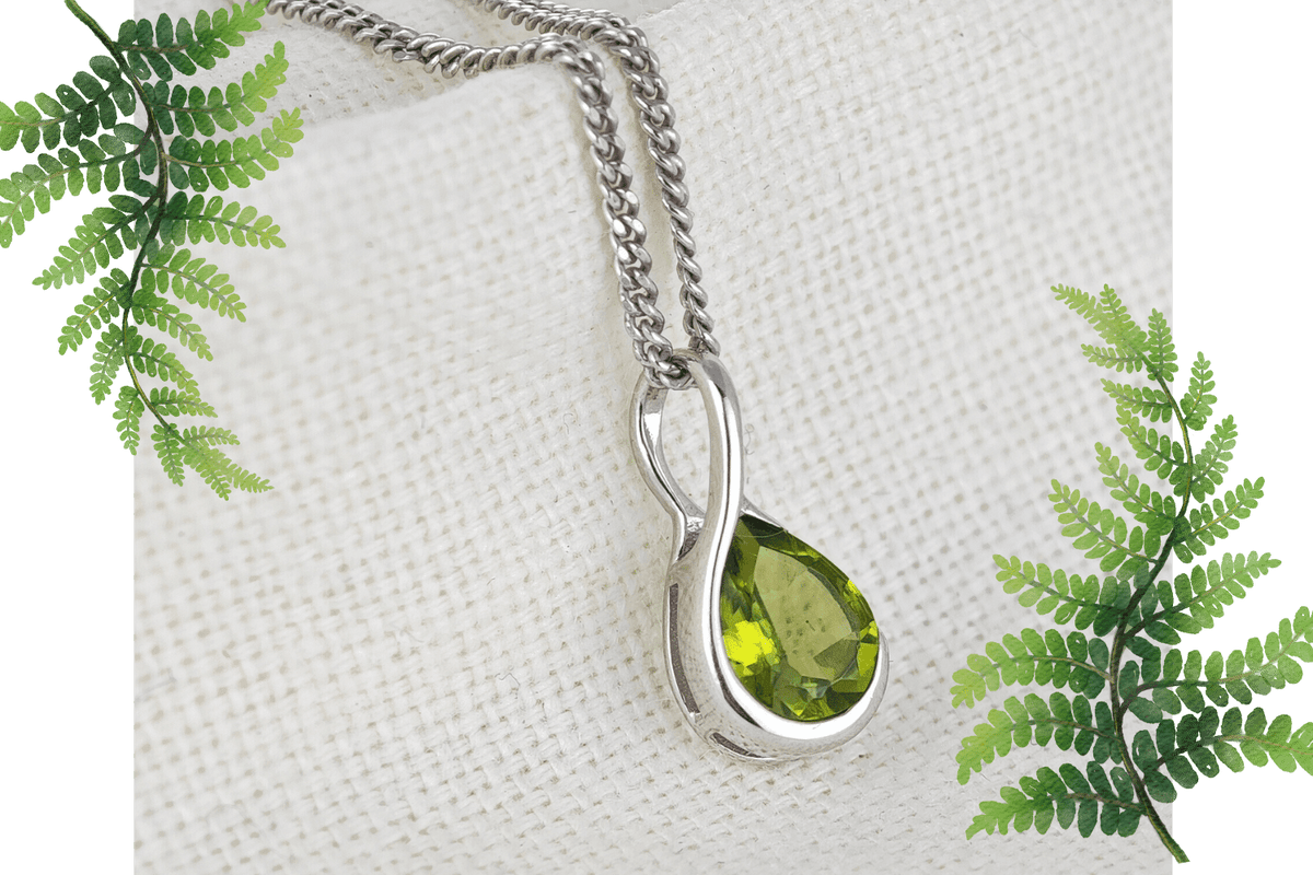 Natural Green Peridot Pendant on Fabric Background flagged by fern leaves