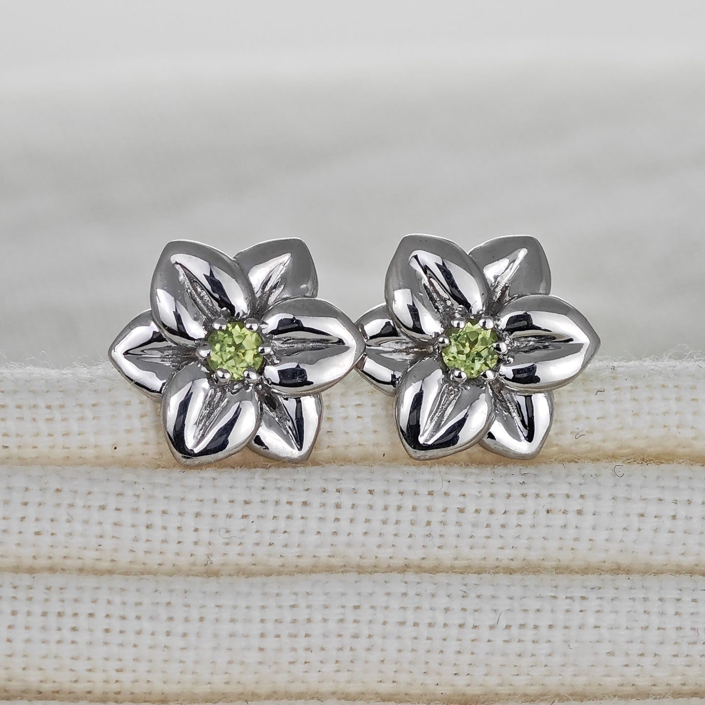 Silver flower-shaped earrings with green gemstones on a fabric surface
