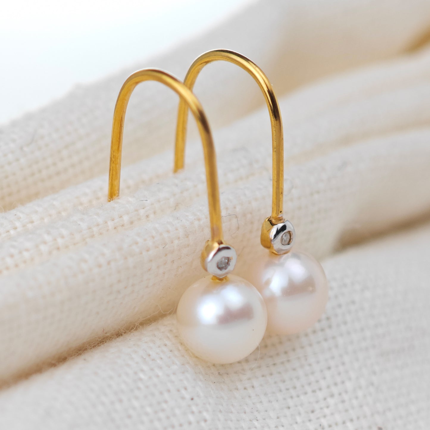 Gold earrings with pearls on a textured beige surface
