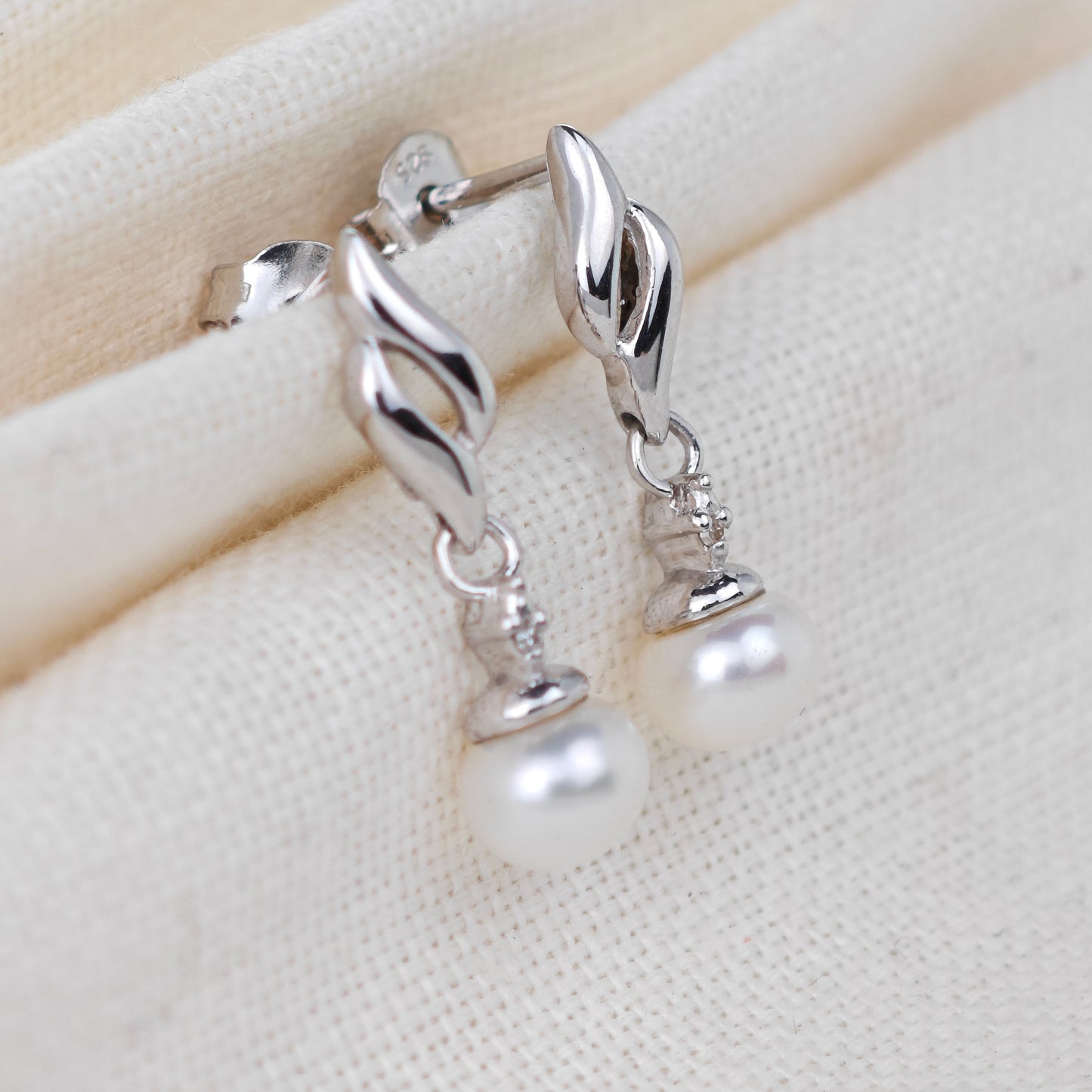 Silver earrings with pearl drops on a beige fabric background