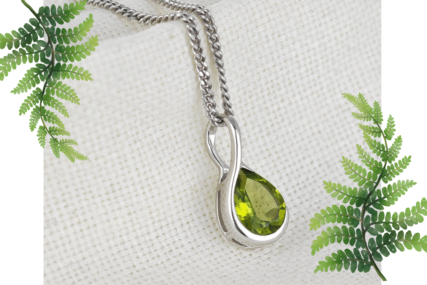 Natural Green Peridot Pendant on Fabric Background flagged by fern leaves