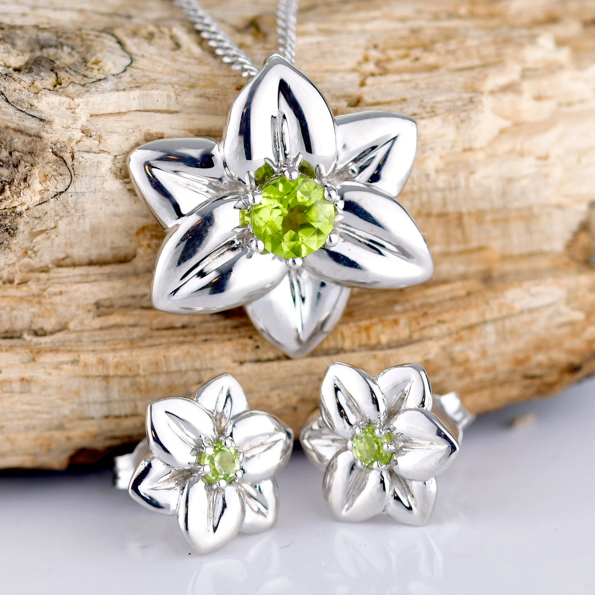 Natural Periodot set Daffodil flower pendant and matching earrings made of sterling silver shown rested on a natural split log