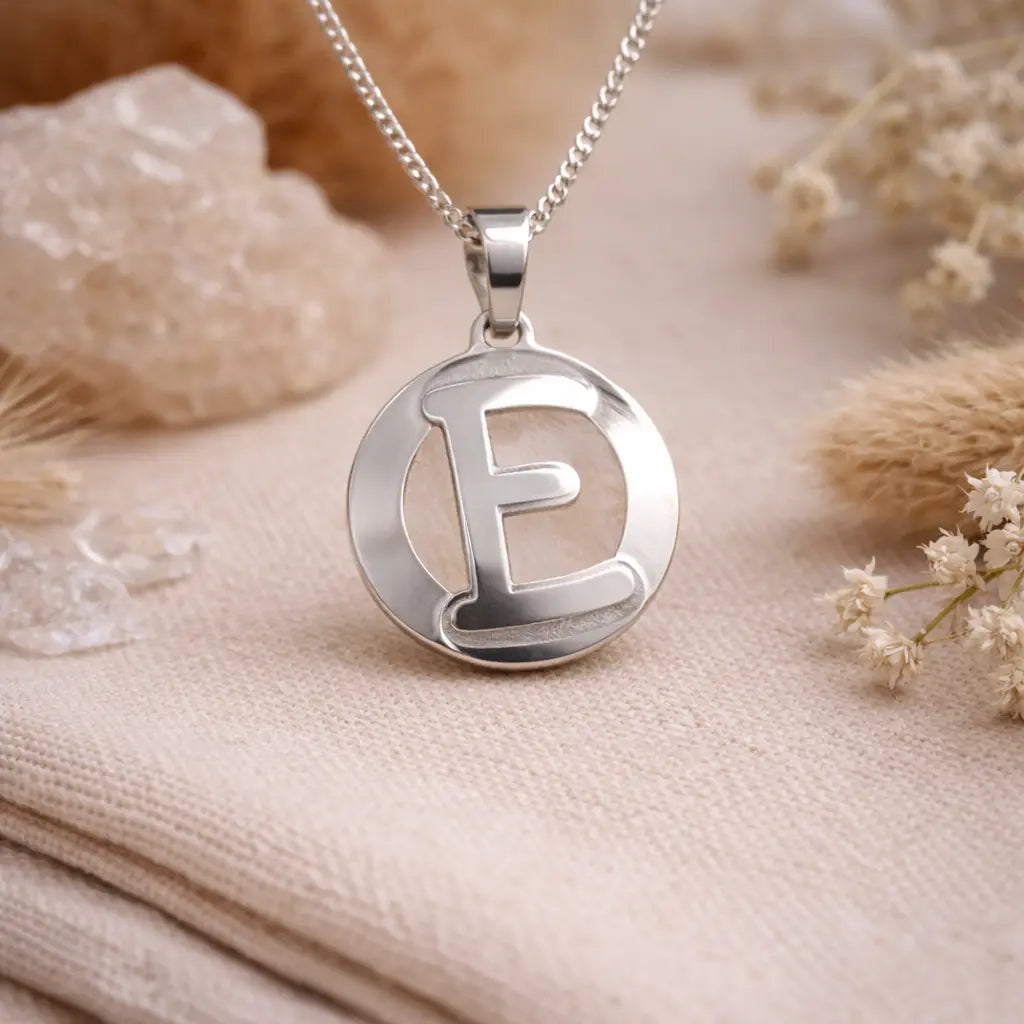 Letter E engraved and cut out initial necklace in recycled sterling silver on neutral background