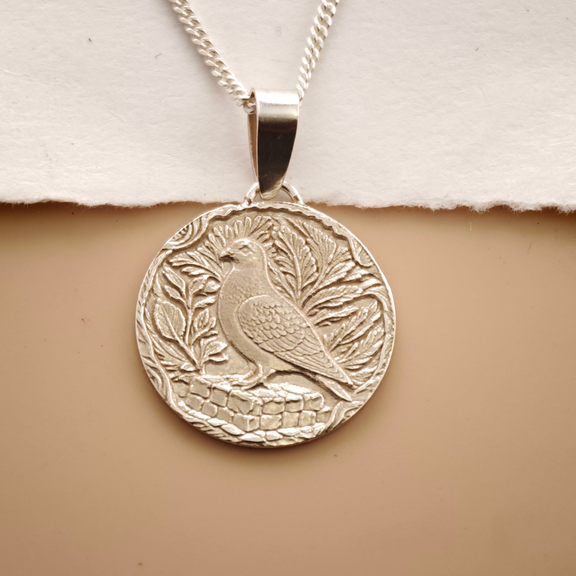 Silver pendant with bird design on a beige background