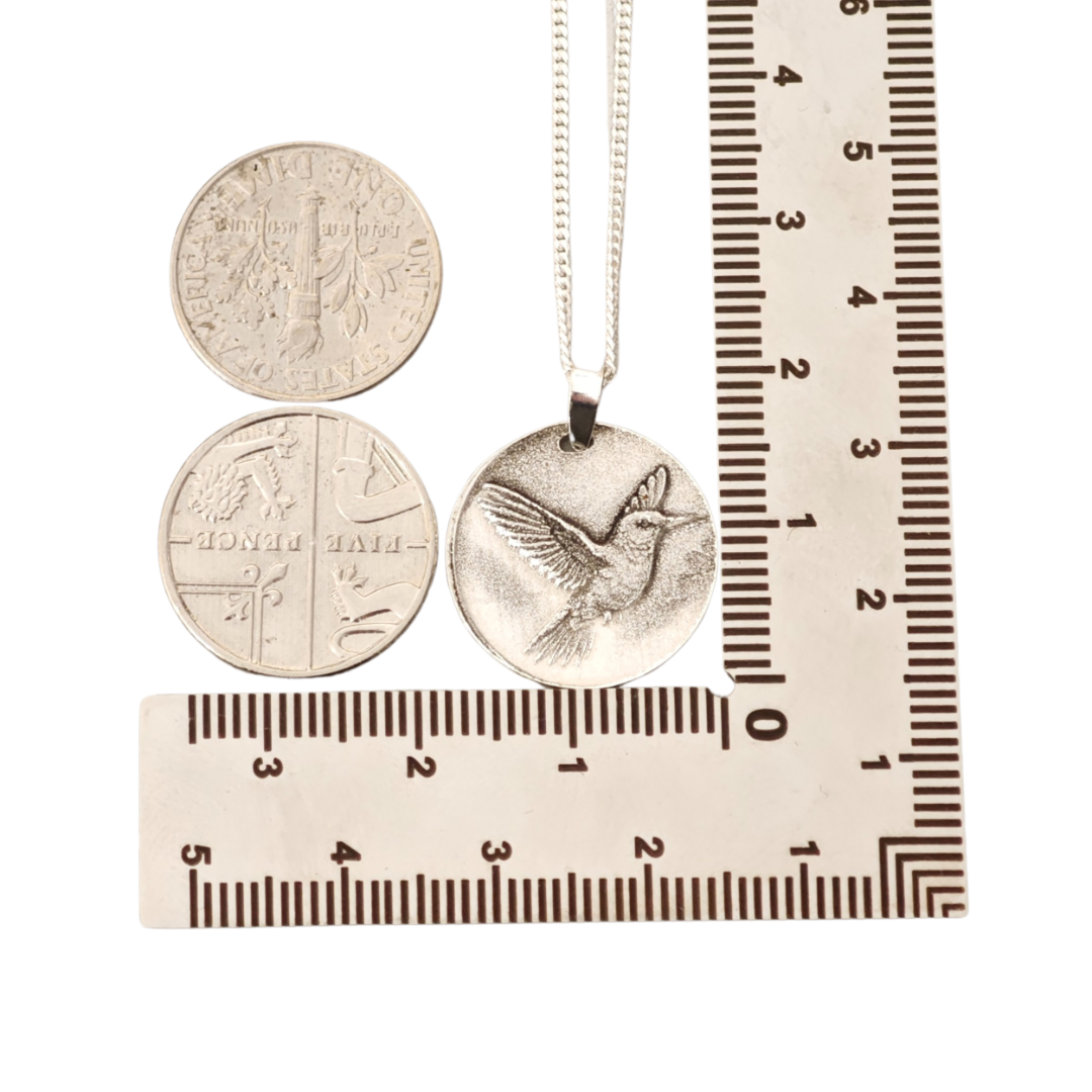 Hummingbird deep engraved sterling silver pendant on curb chain shown against ruler and coins
