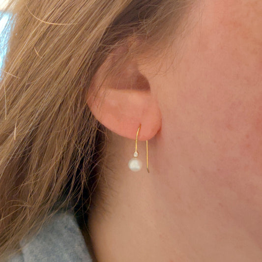 Pearl earrings with gold hooks and small diamonds on ear