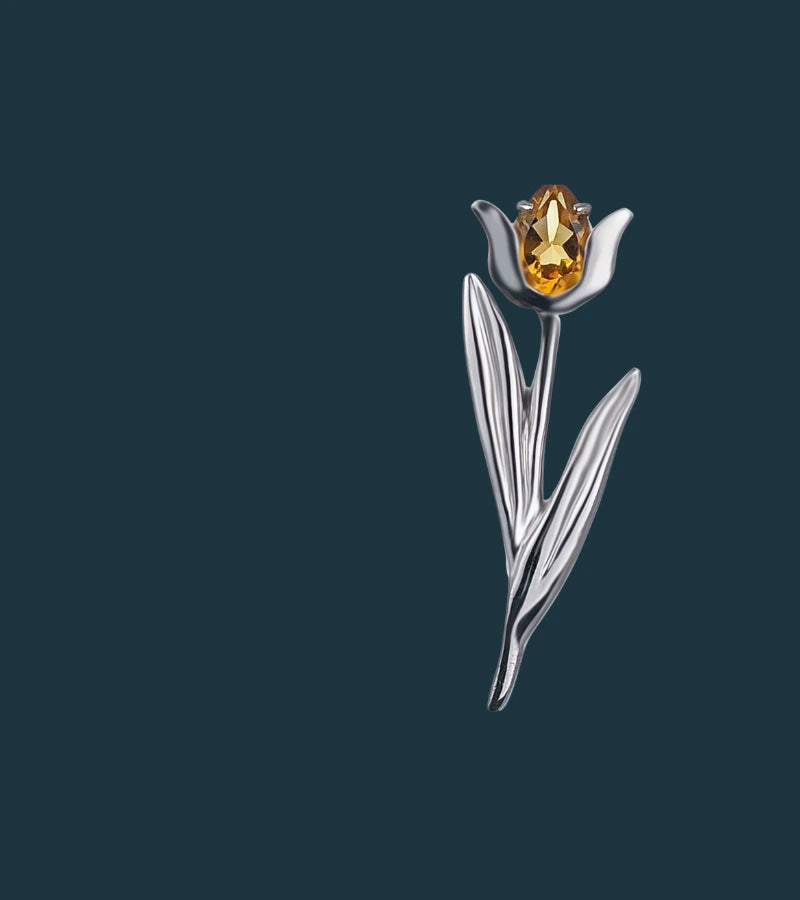 Silver tulip-shaped brooch with a yellow citrine on a dark background