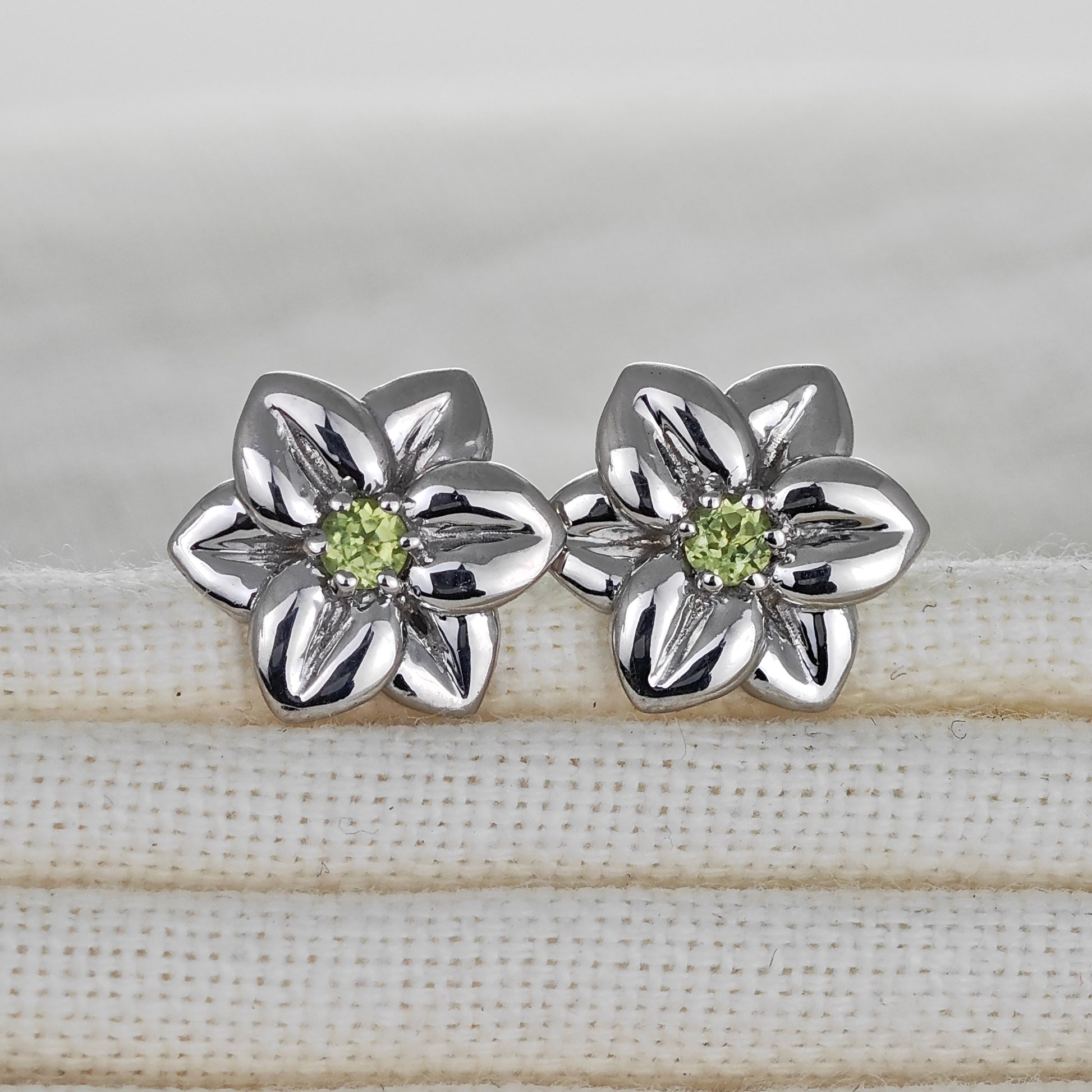 Silver flower-shaped earrings with green gemstones on a fabric surface