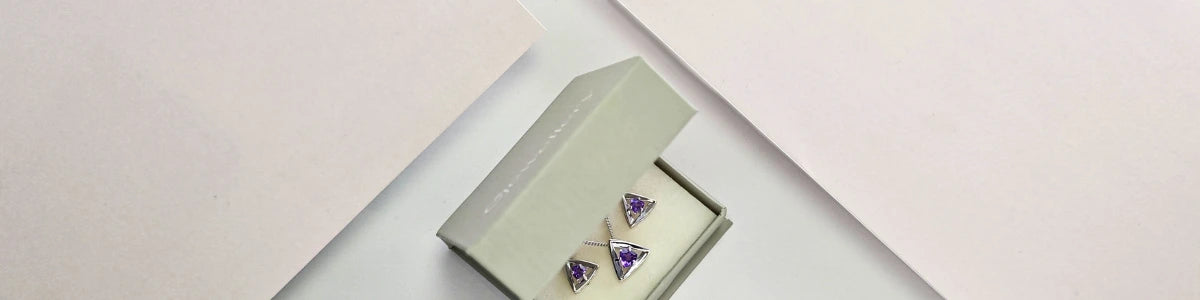 Pair of purple triangle earrings and matching necklace in a green jewellery box on a light pink background