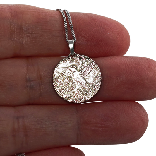 Silver pendant with intricate design held between fingers on a white background