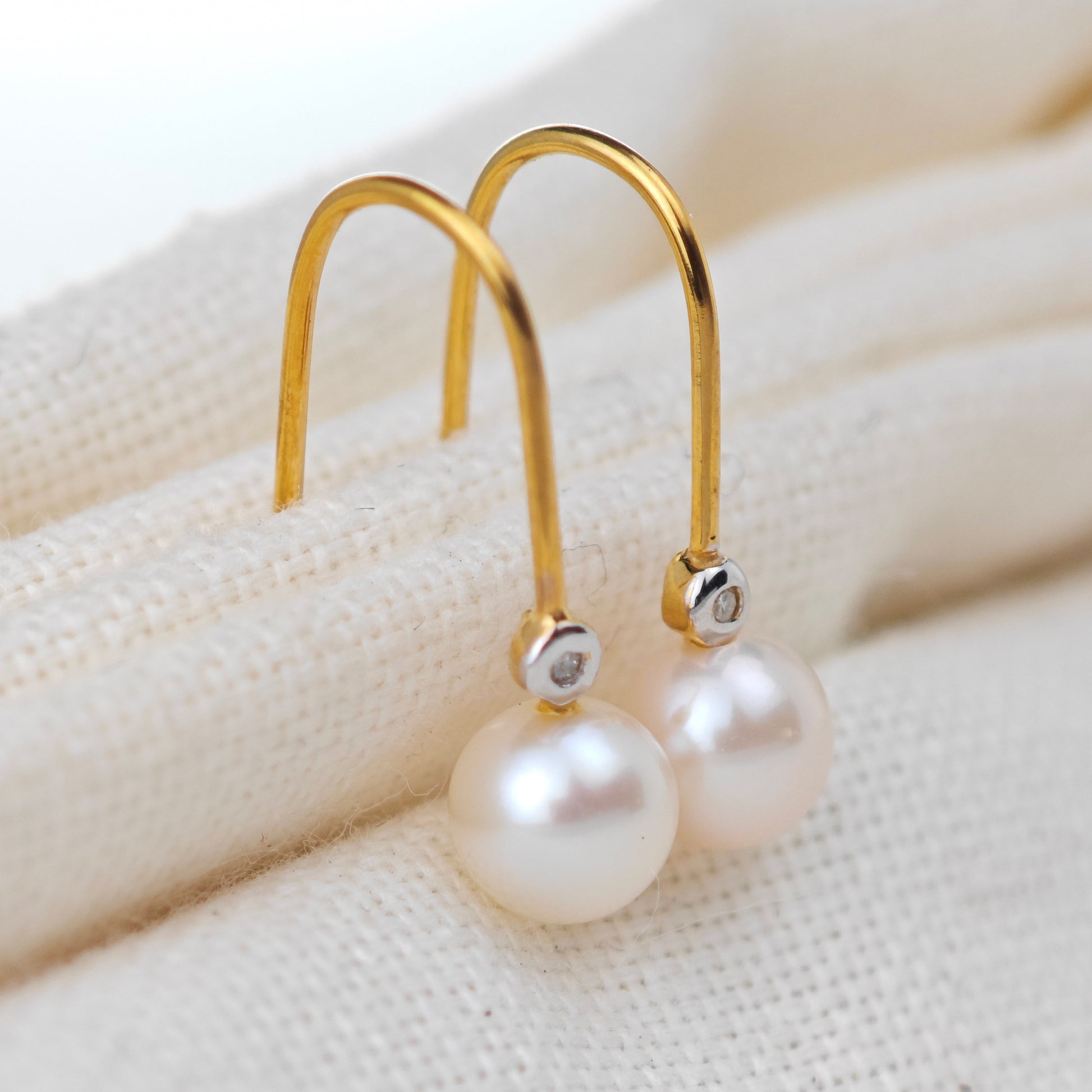 Gold earrings with pearls on a textured beige surface