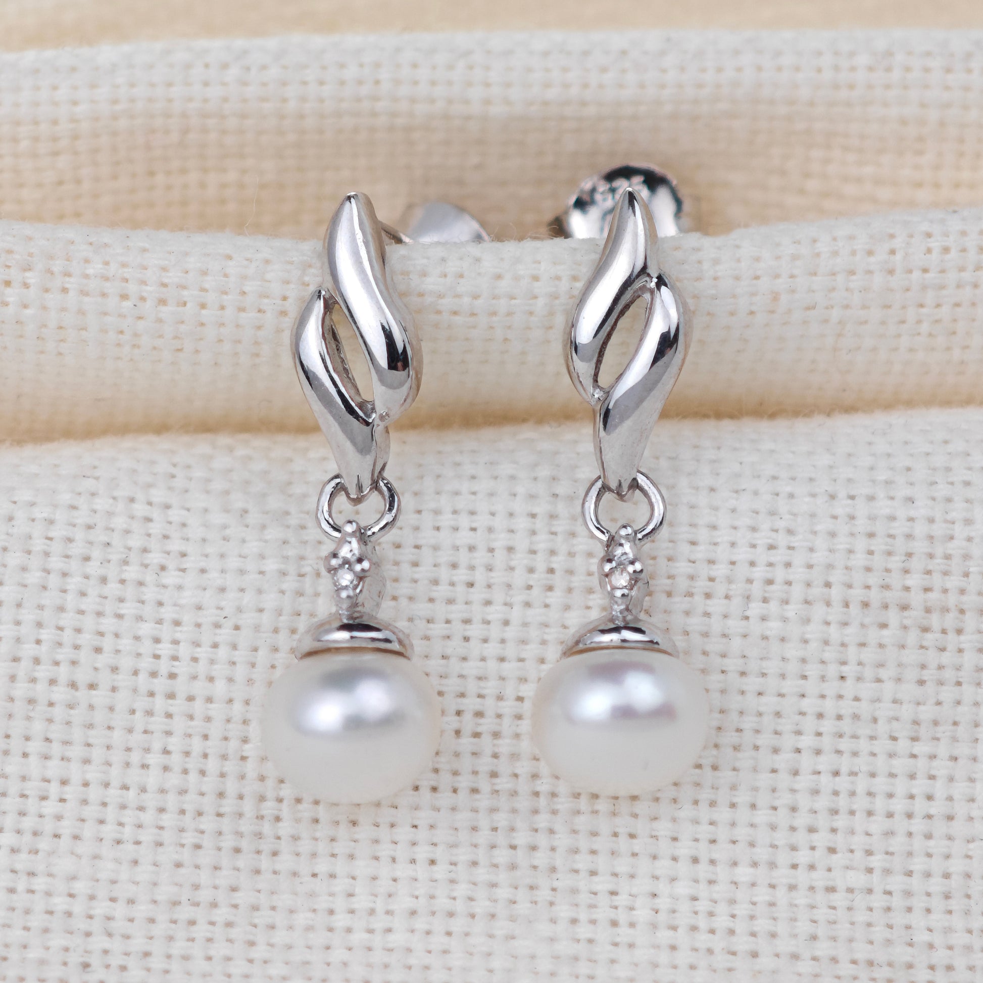Silver earrings with pearl drops on a beige fabric background