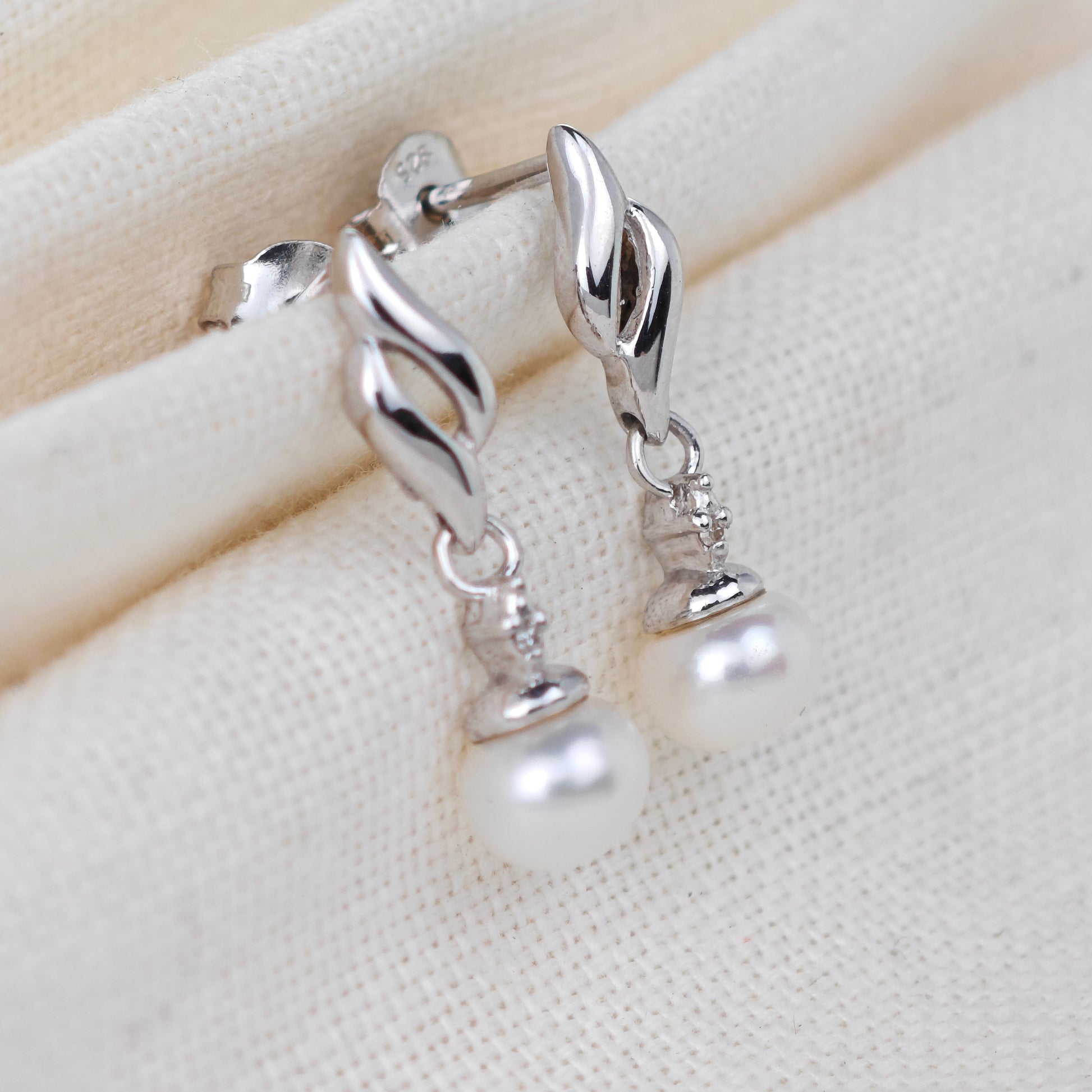 Silver earrings with pearl drops on a beige fabric background