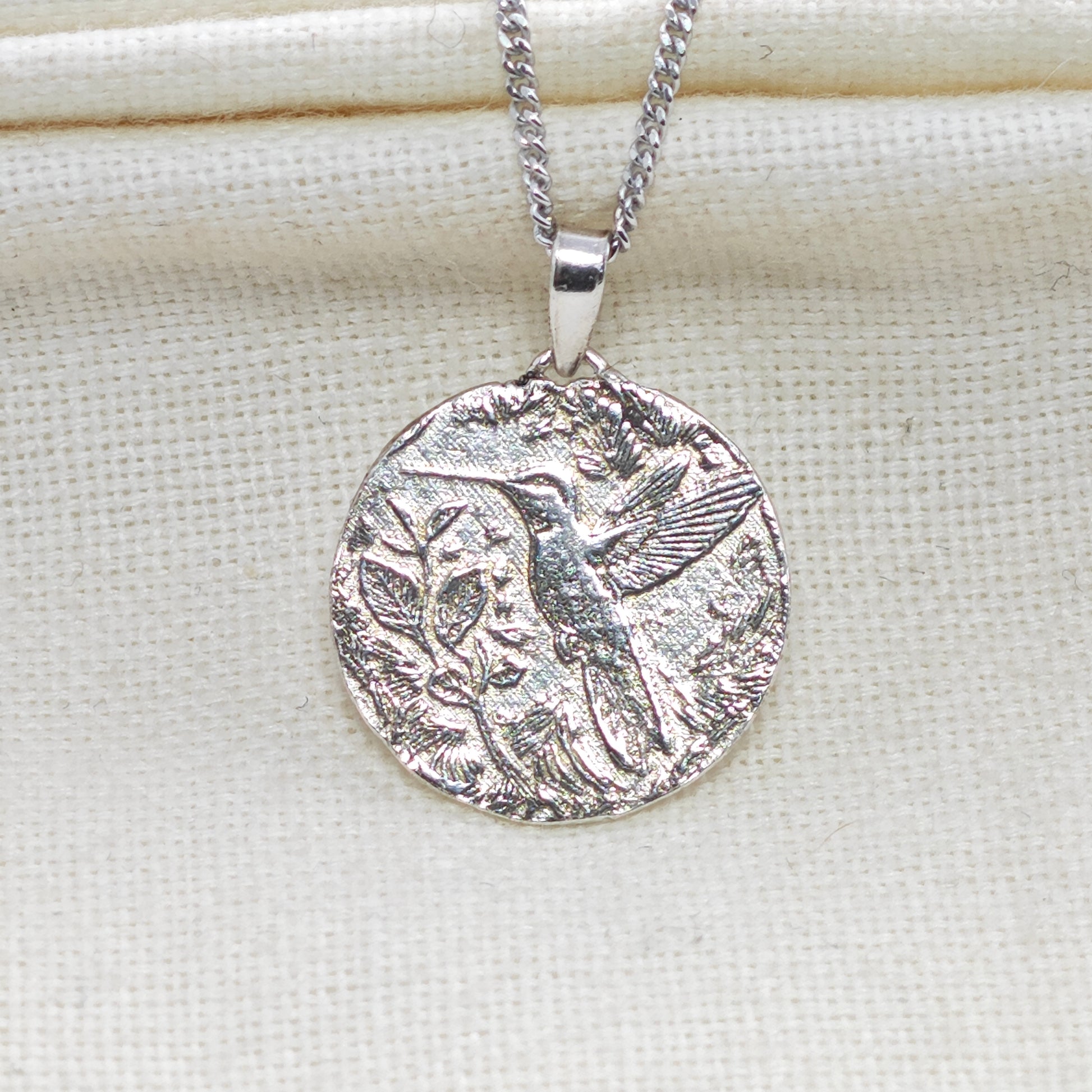 Silver pendant necklace with intricate design on a light fabric background