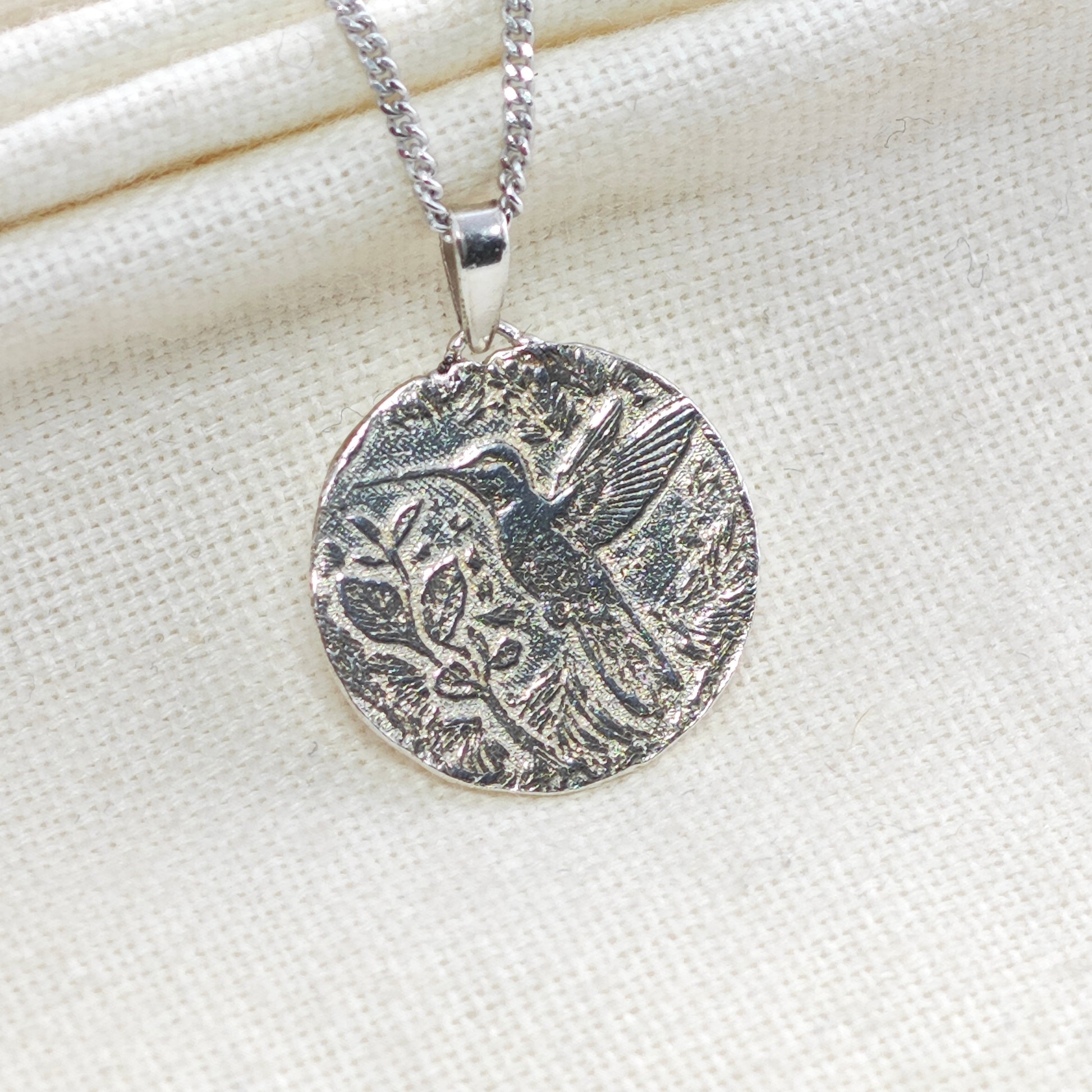 Silver pendant necklace with bird design on a white fabric background