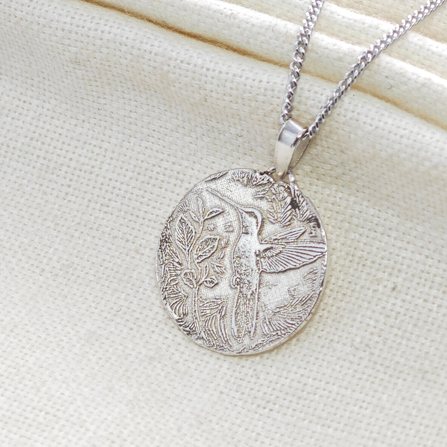 Silver pendant necklace with intricate design on a light fabric background