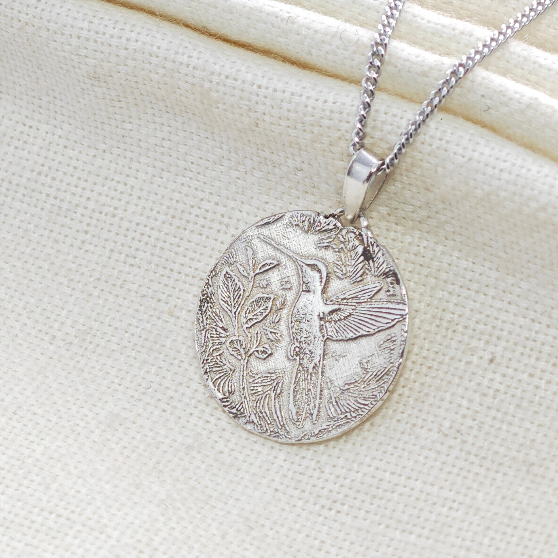 Silver pendant necklace with intricate design on a light fabric background