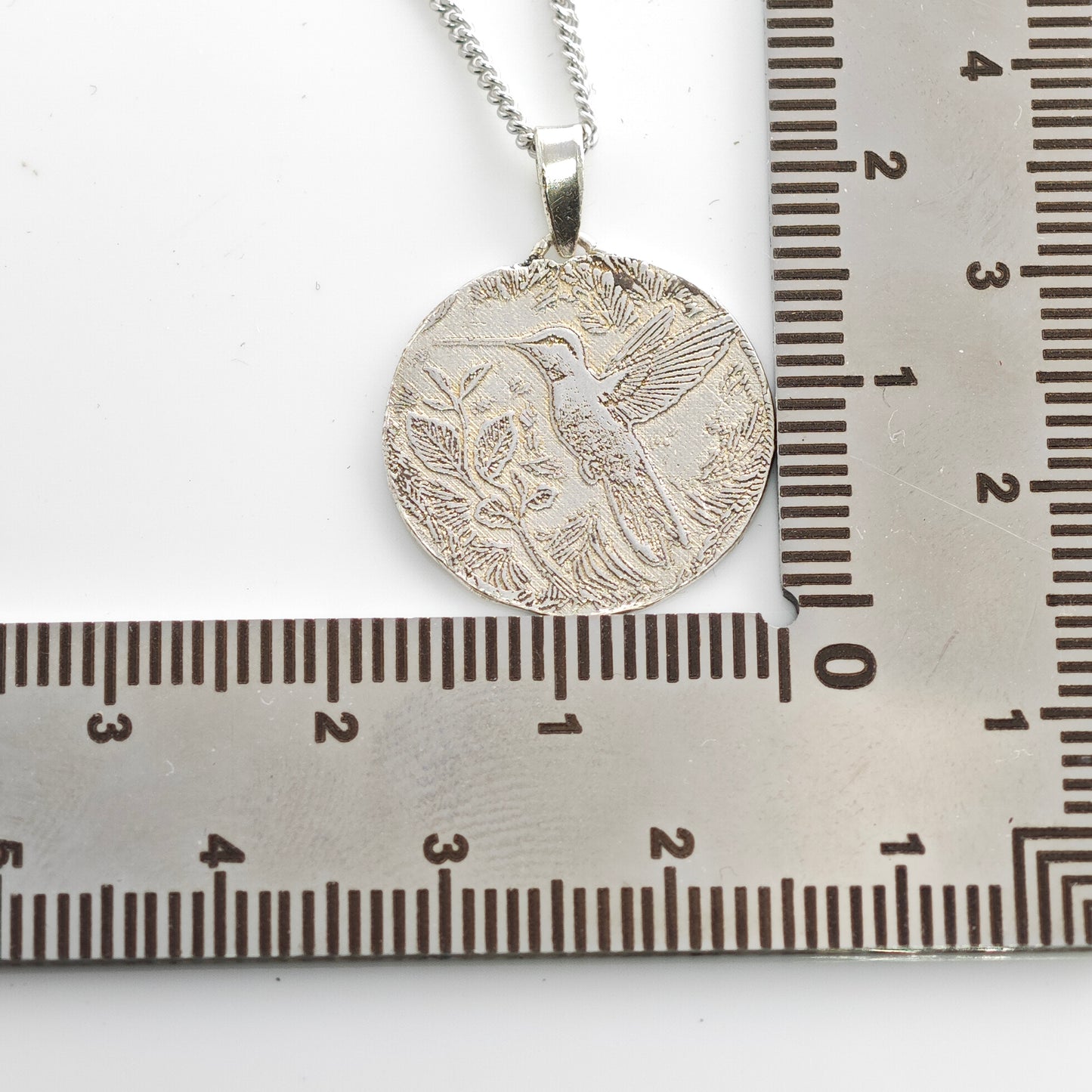 Silver pendant on a chain next to a ruler for scale
