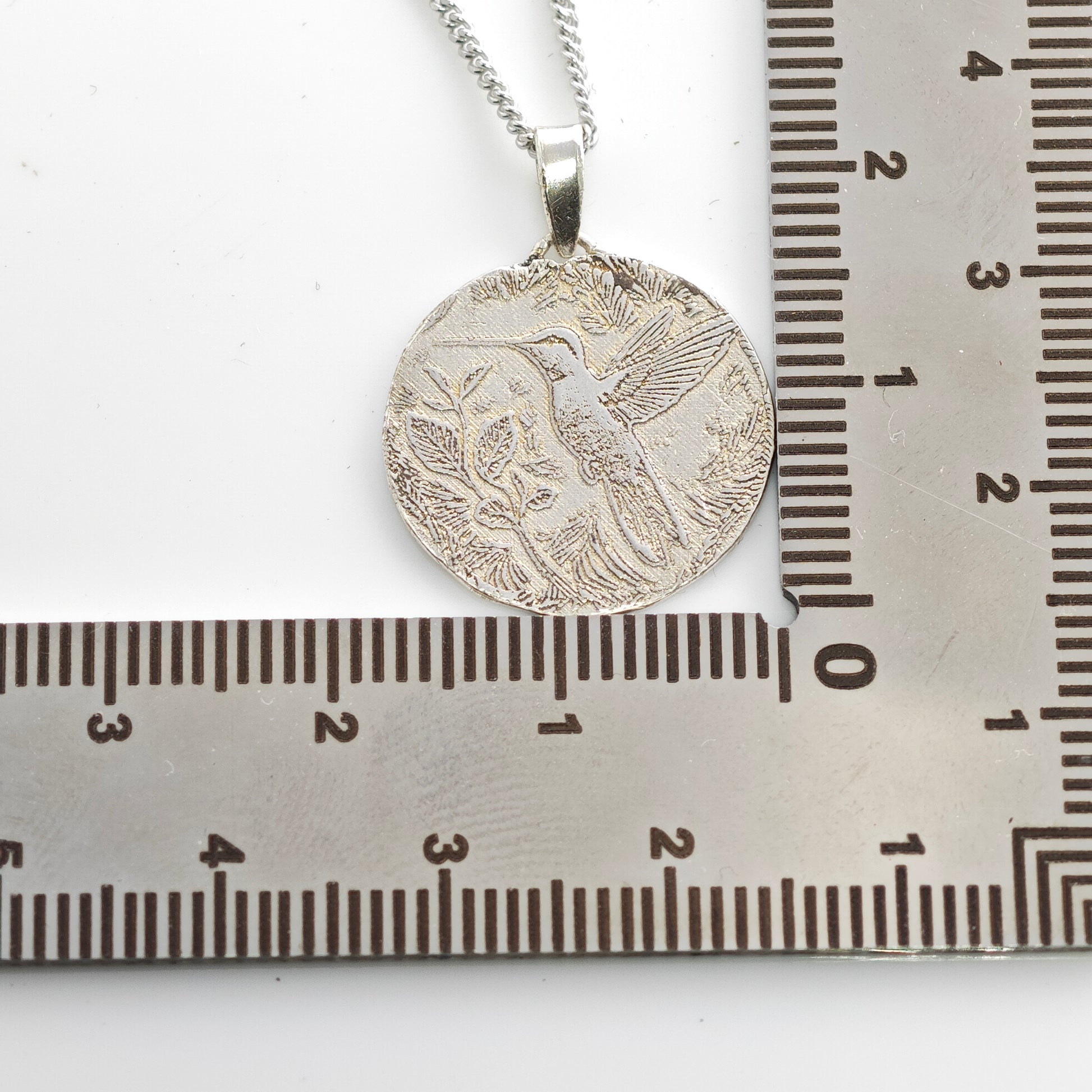 Silver pendant on a chain next to a ruler for scale