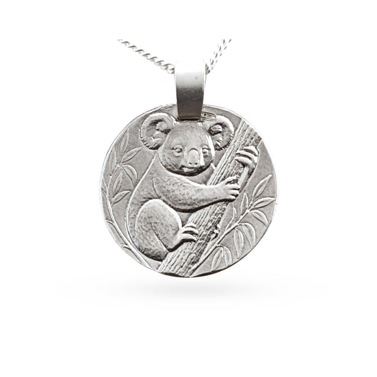 A round silver pendant necklace featuring an embossed koala clinging to a tree branch, suspended from a silver chain against a plain white background.